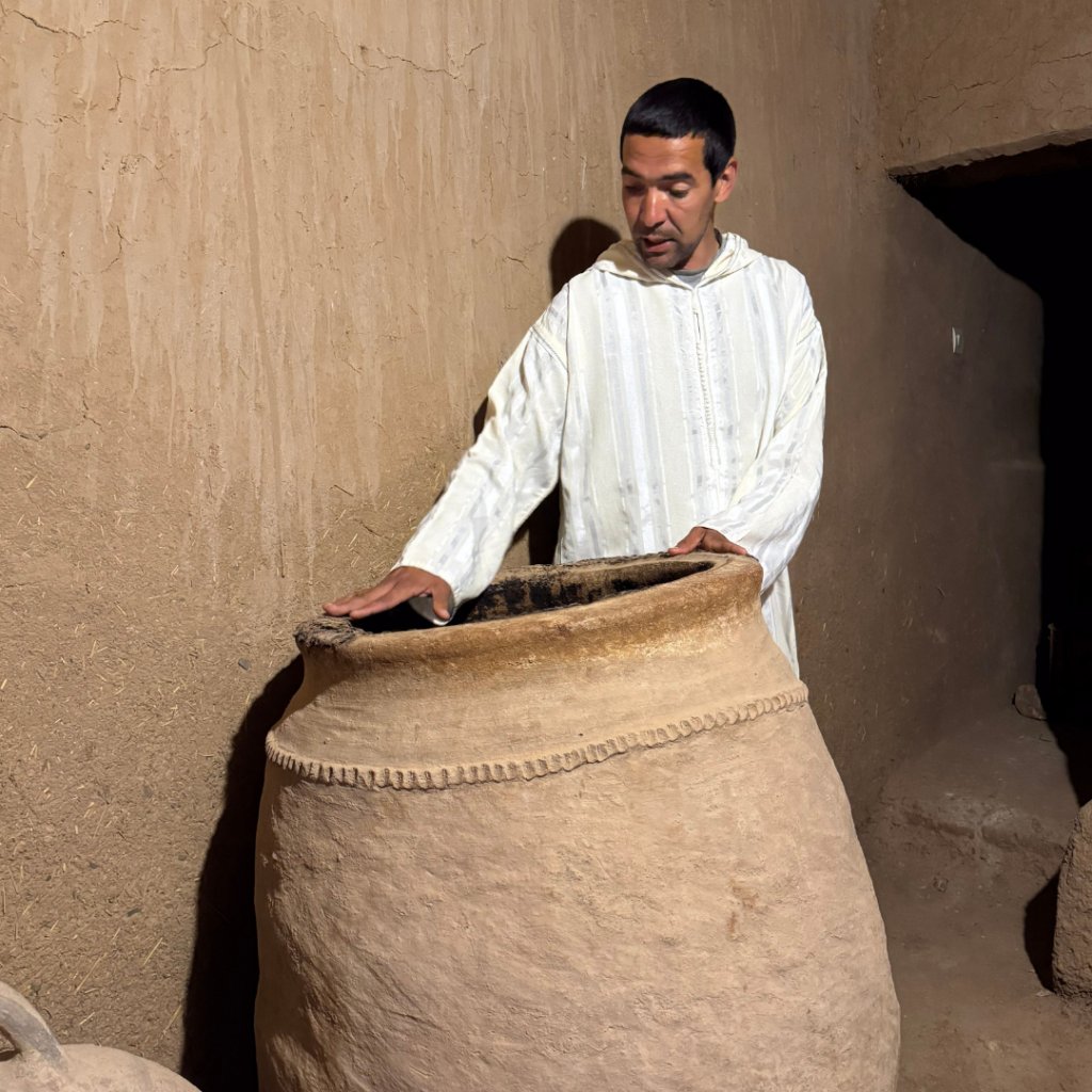 Artisan marocain en gandoura blanche observant une grande jarre en terre cuite dans une kasbah traditionnelle d’Aït Ben Haddou.