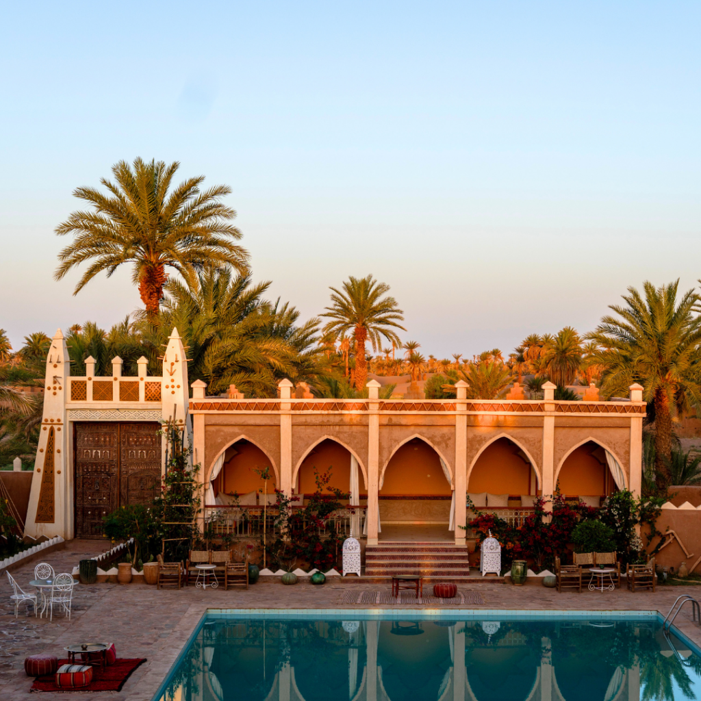 Vue de l’hôtel Sbai Palace à M’Hamid avec piscine, palmiers et architecture traditionnelle marocaine au lever du soleil
