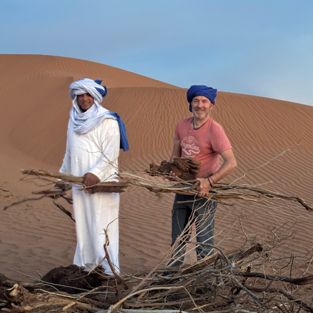 Deux hommes ramassant du bois dans les dunes de M’Hamid, symbole d'une immersion locale dans la vie nomade du désert.