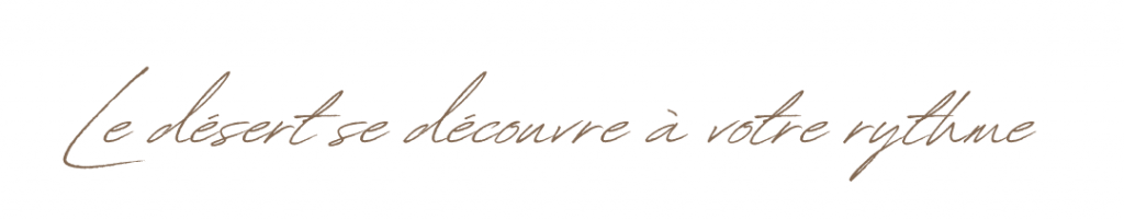 Slogan manuscrit "Le désert se découvre à votre rythme" écrit en calligraphie élégante beige sur fond blanc.