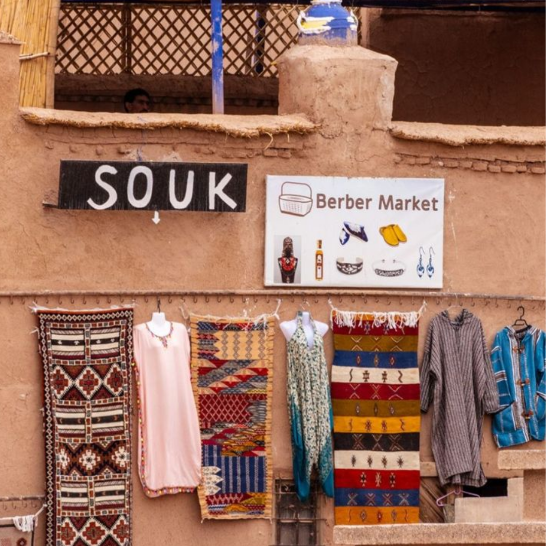 Façade d’un souk berbère traditionnel avec tapis colorés, vêtements et enseigne artisanale